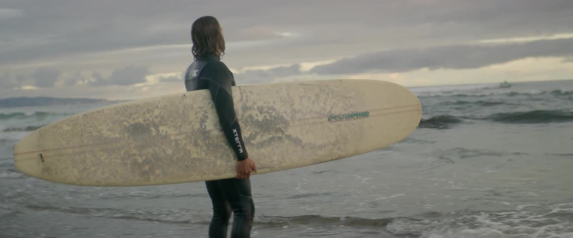 A surfer carries his surfboard on the beach