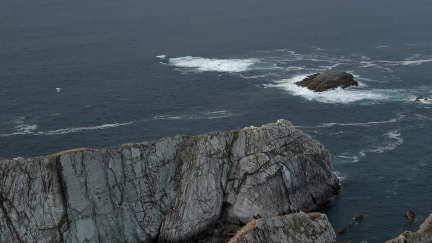 Bird flying above a sea next to large rocky hills