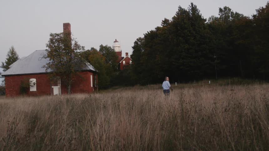 Woman in a field walking towards a lighthouse