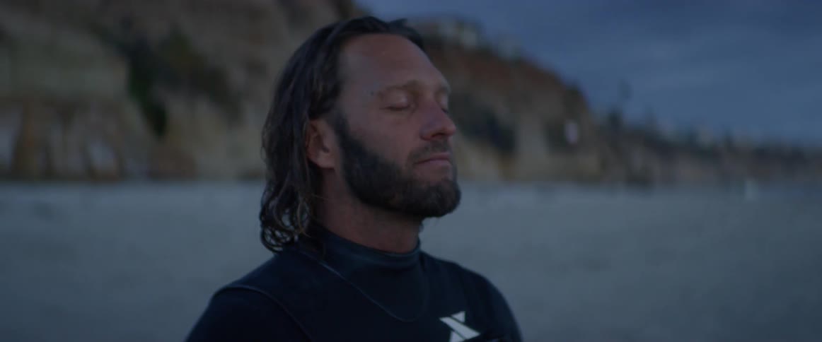 A male surfer meditating beside the water
