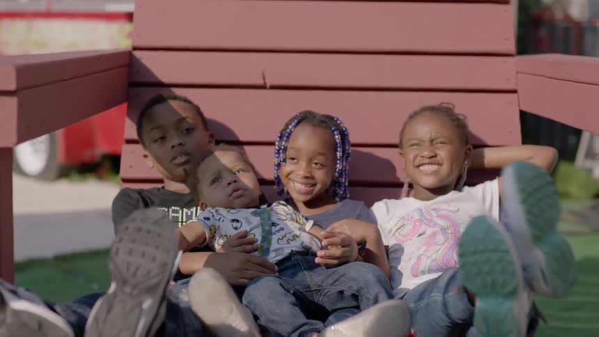 Three children sit in a large chair holding a baby