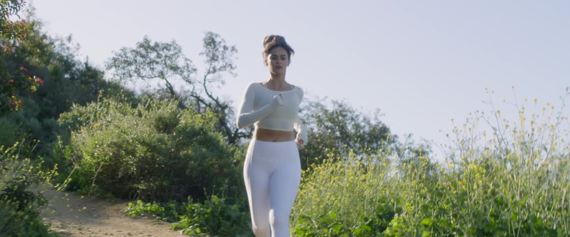 A woman is running along a dirt path lined with shrubs