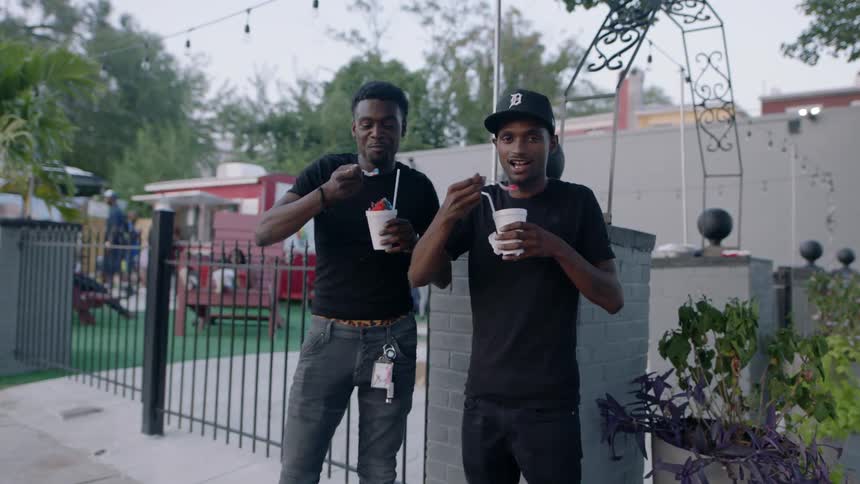 Two men enjoy colorful snow cones outside a food park