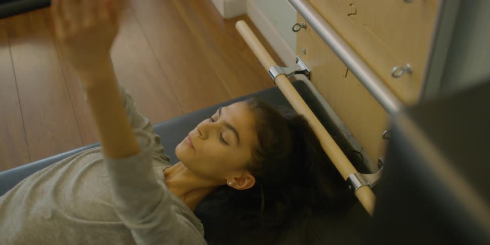 A woman laying on mat with arms straight, curls upward