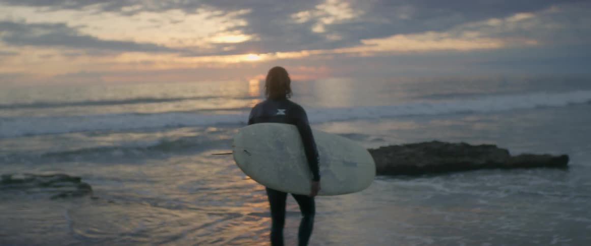 Man carries a surfboard and walks on the beach