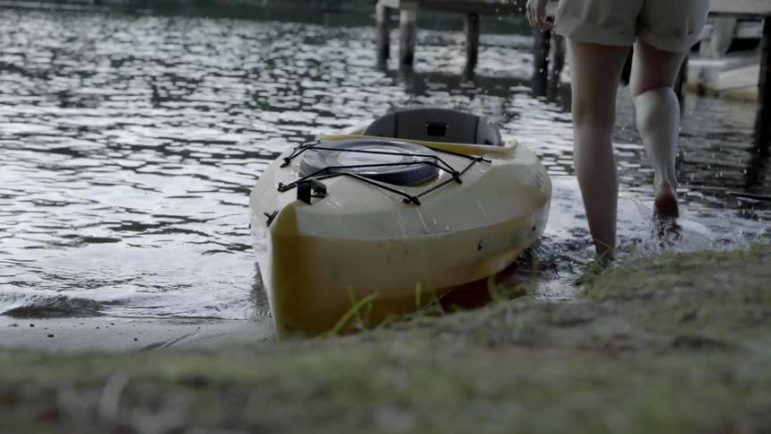 A woman holding an oar climbs into a kayak