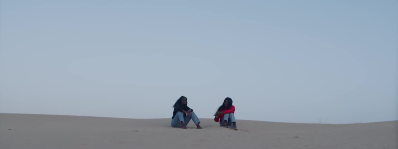 Two women seat themselves on the sand in a desert