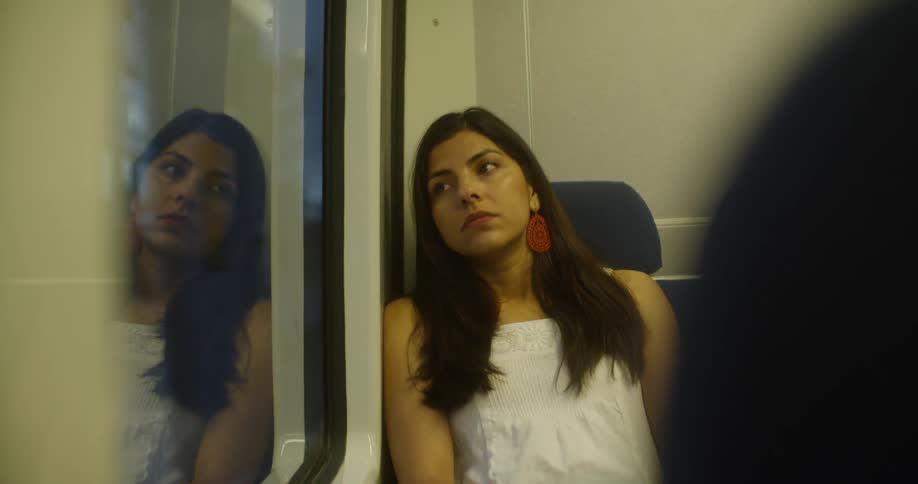 A young woman in a white blouse sits back in her bus seat and lays her head against the wall