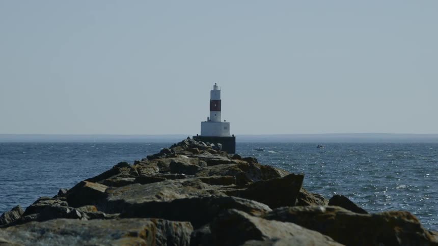 A lighthouse sits at the end of the rocky shore