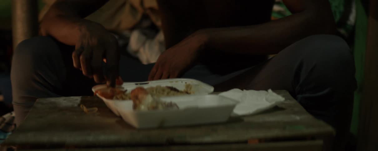 A young man stirs his food before picking a large piece of chicken from the top then continues stirring