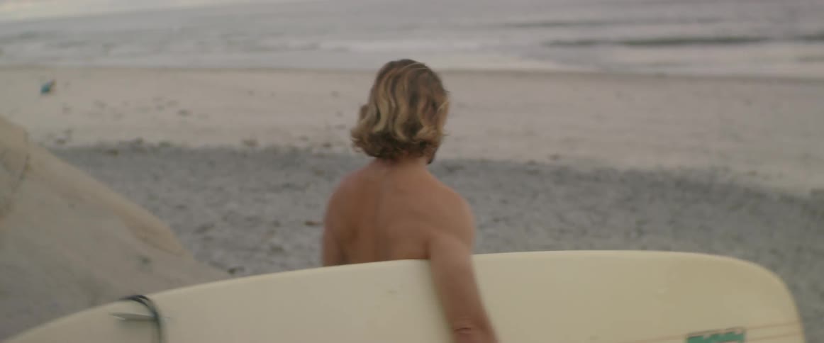 A man walks along the beach carrying a surfboard