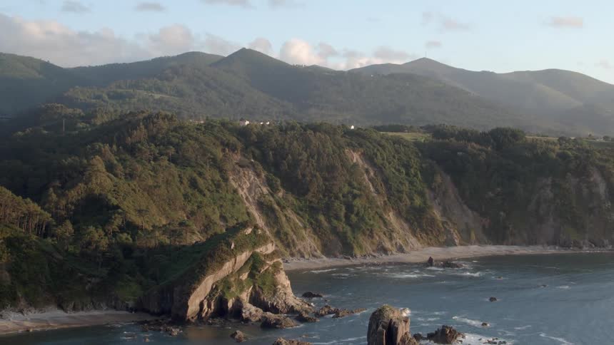 The sea waves crashing on a beach next to a big mountainous region