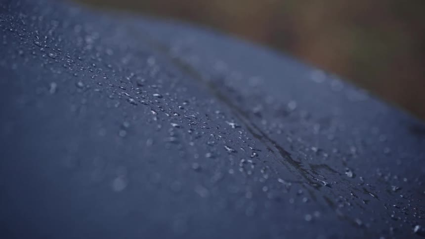 Drops of liquid sitting on a smooth dark purple and curved surface moving slightly side to side