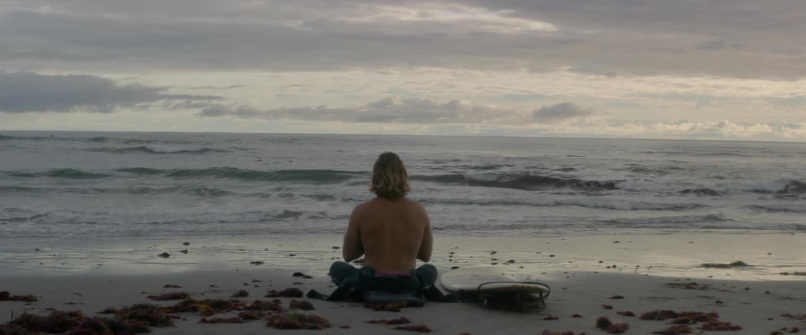 Man sitting on a beach next to his surfboard