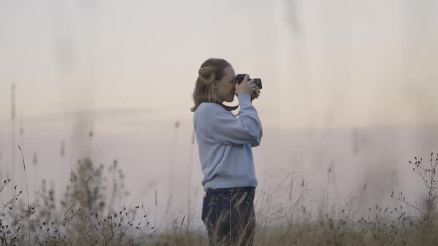 A young woman looks through her camera in a field