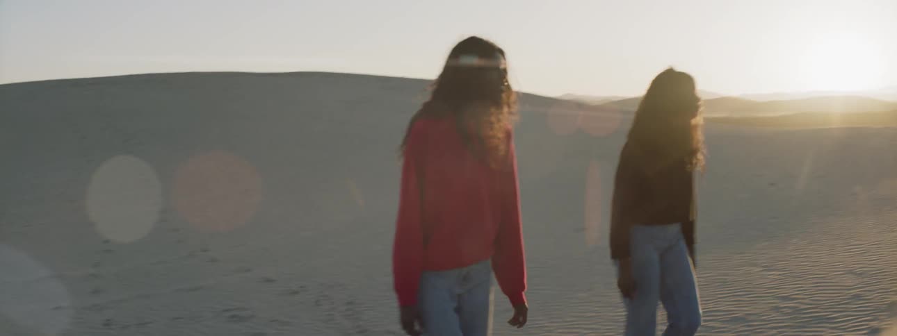Two women walk through a desert at sunrise
