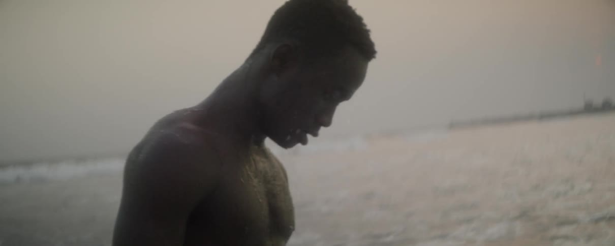 A man covers his face with his hands then splashes himself with water as he walks through the ocean