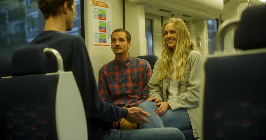A man sits on a bus talking to another man and a woman