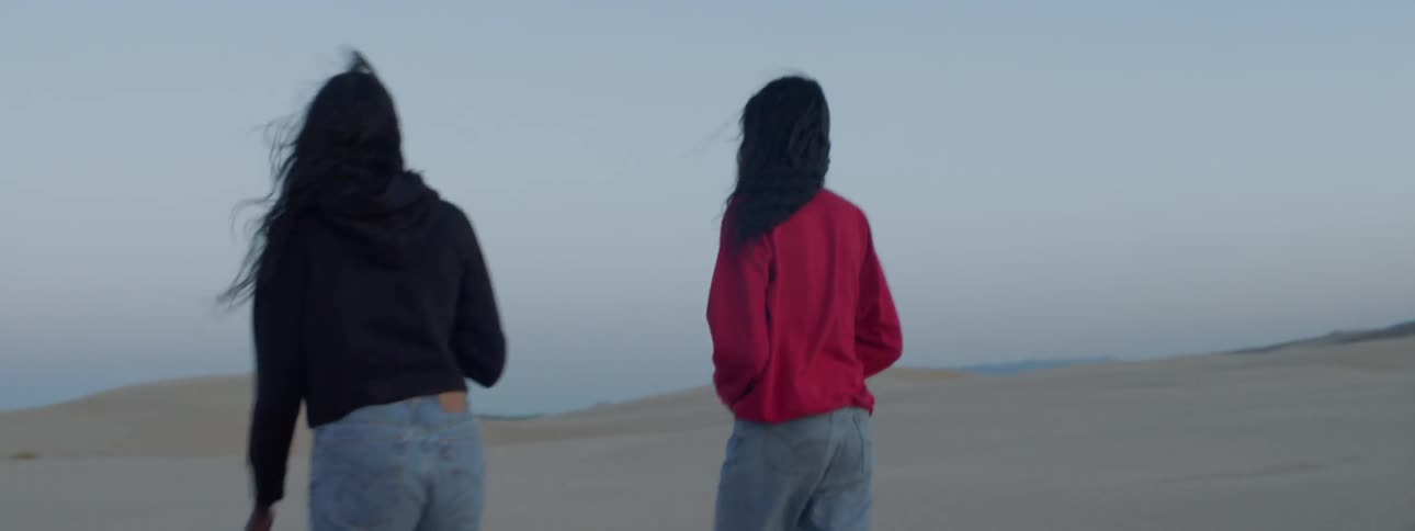 Two women walking around in the sand dunes wearing jeans