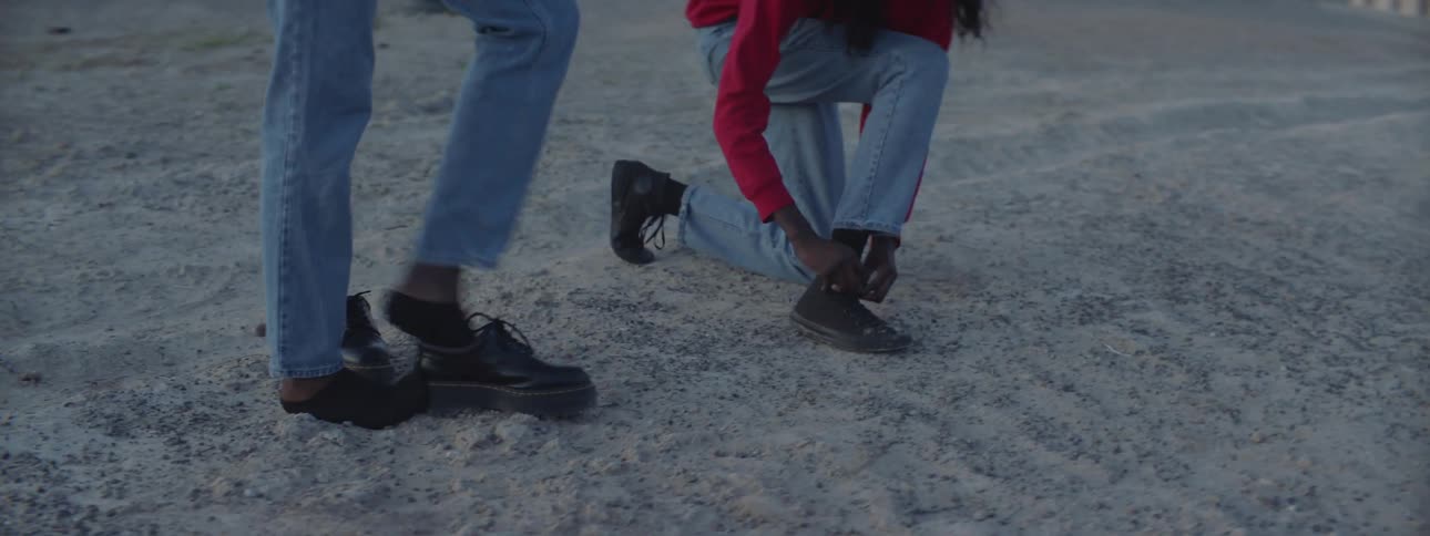 A woman tying shoes and another takes her shoes off on the beach