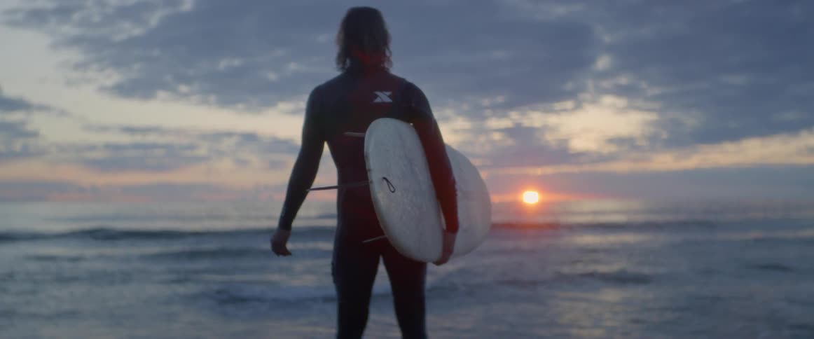 Man looking at the sun rise while holding his surfboard