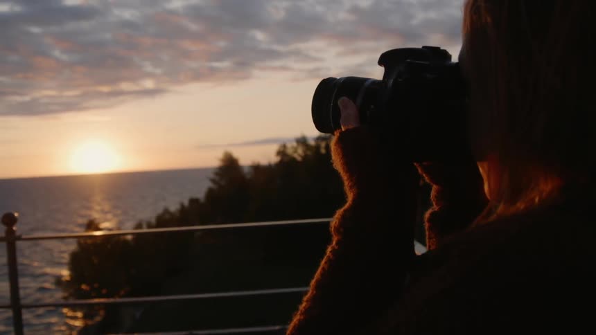 Woman taking a picture of the sea at sunset
