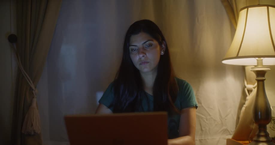 A woman sits on a laptop in the lamplight at night