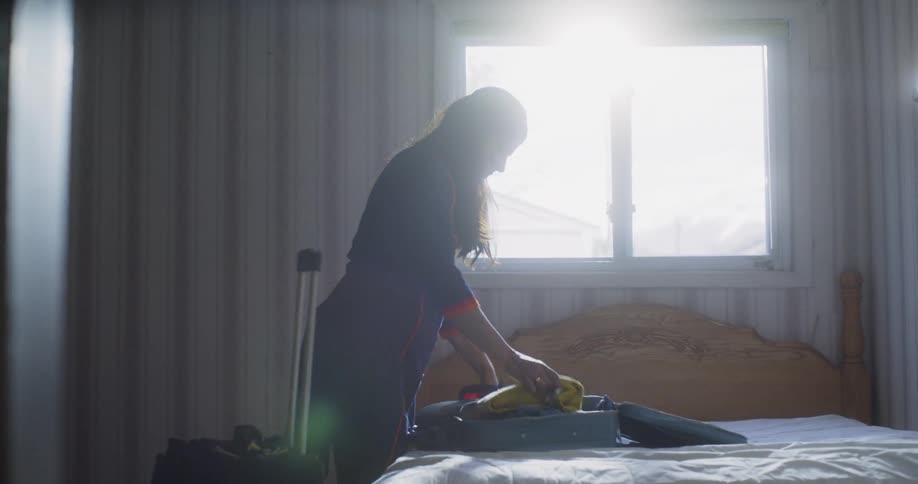A woman picks items out of a suitcase and shakes them out in the sunlight