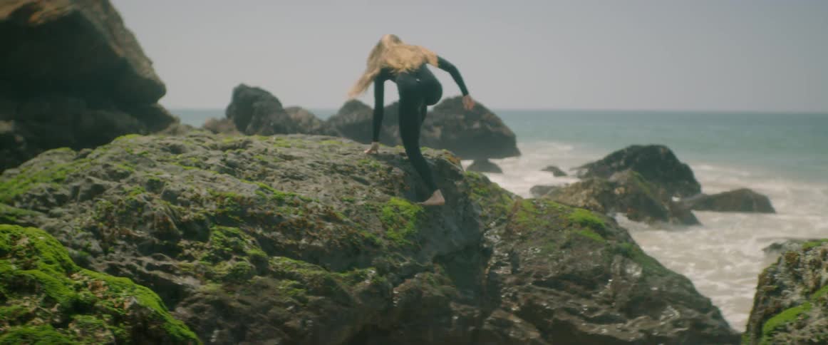 Woman surfer climbing on a rock and sitting down