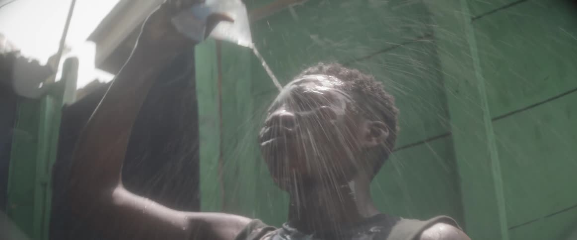 A man squirts water over his head and then takes a drink from the container
