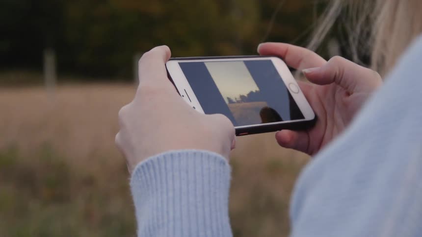 A woman flips through pictures on her phone as she stands in the countryside
