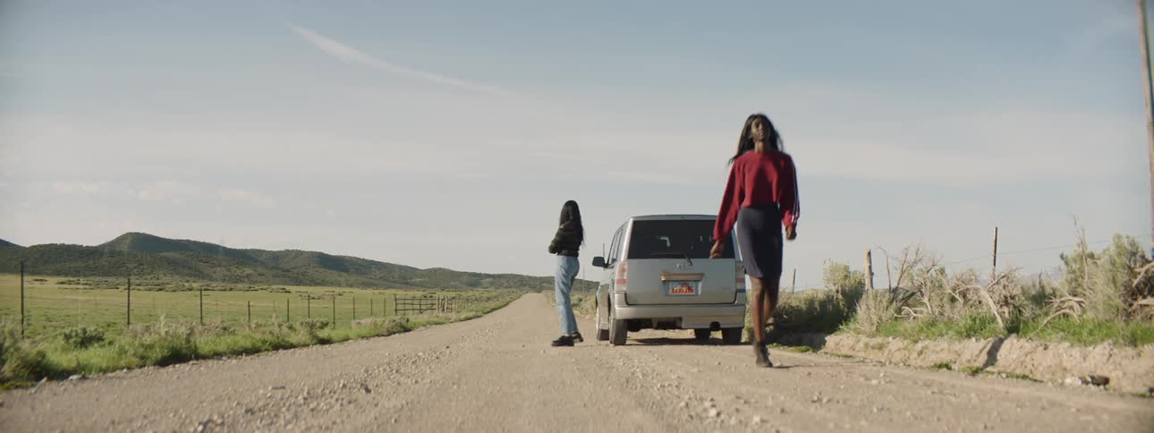 Two women stand by a car parked on a highway before one of them walks away