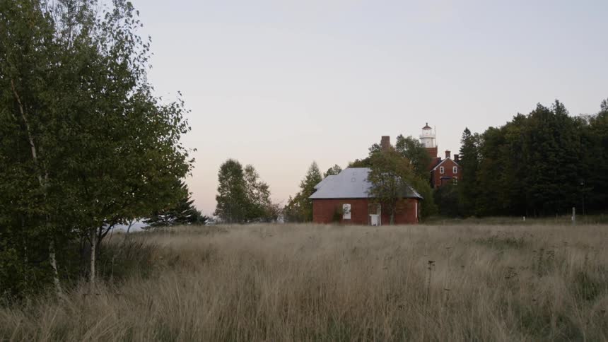 A red building stands alone in a field surrounded by trees