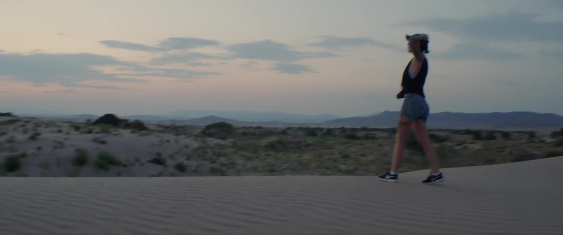 A woman walks through a sandy area at sunset with her hands on her head