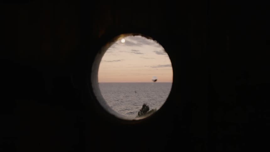 The sunset above the ocean is showing through a hole in a wooden wall