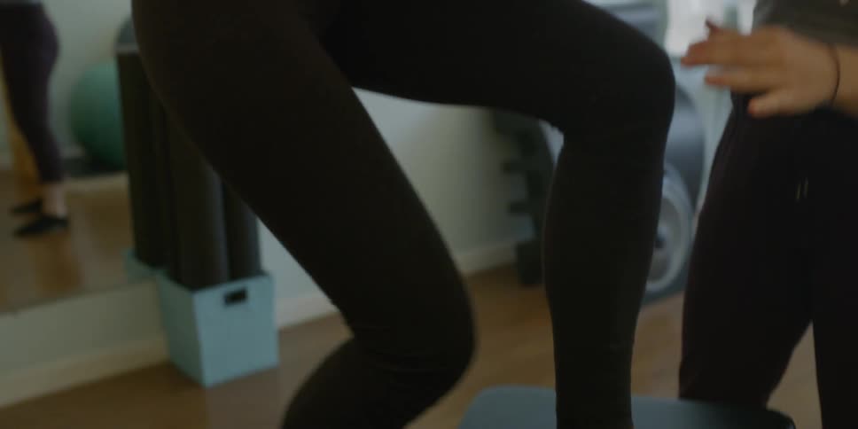 Woman exercises legs while other woman holds her arm