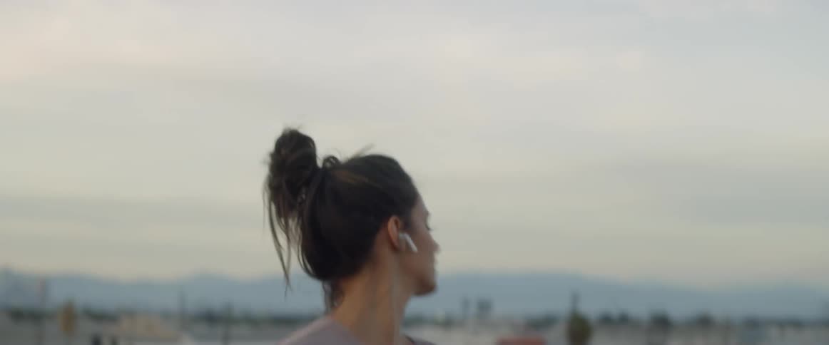 A woman twirls and dances on a rooftop as she listens to music