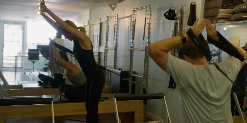 A female trainer gives instructions as three people watch her and try to do as she does