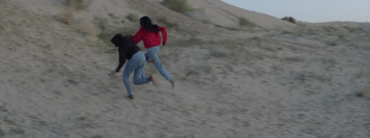 Two women run along the sand going uphill