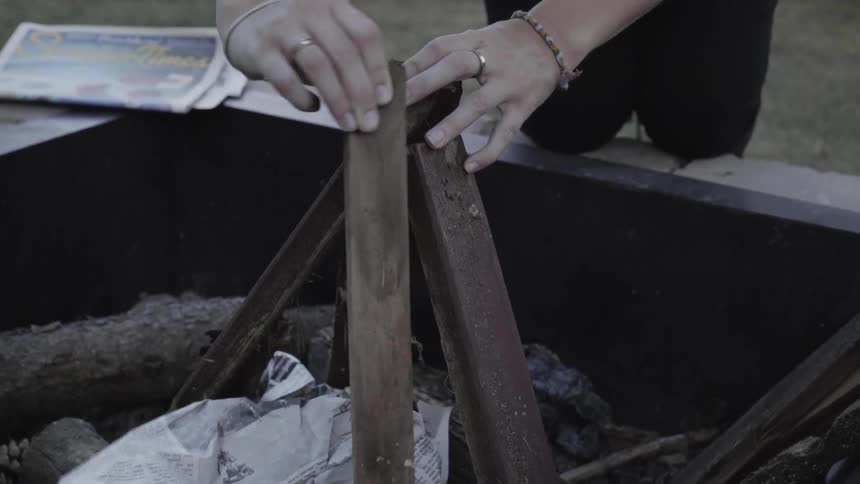A person piles sticks together in a tip to start a fire then rubs their hands