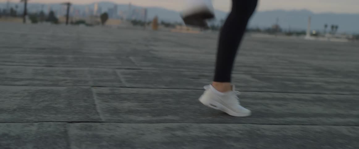 A woman wearing leggings and sneakers is doing ballet in a parking lot