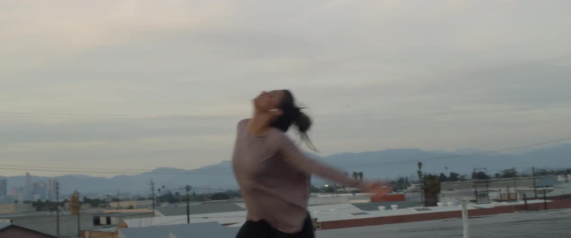 A woman twirls and dances on a rooftop as she listens to music