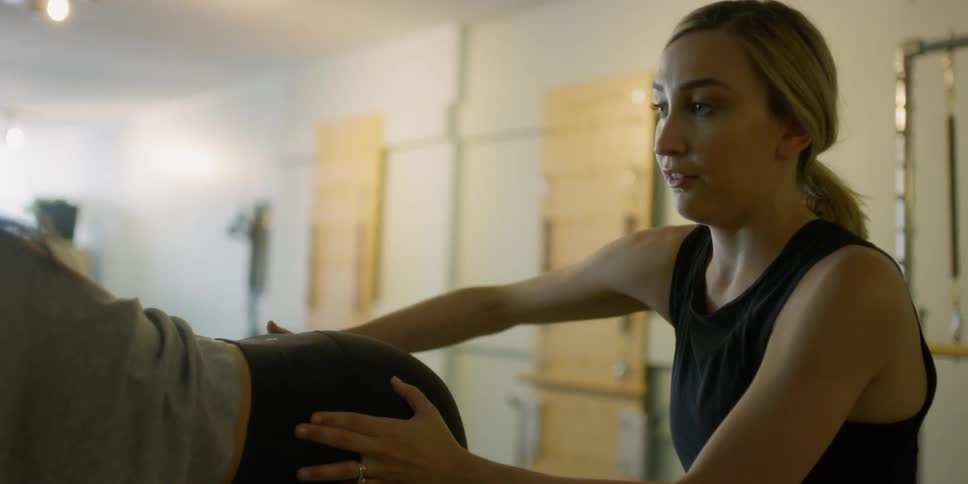 A woman is guided in stretching by an instructor