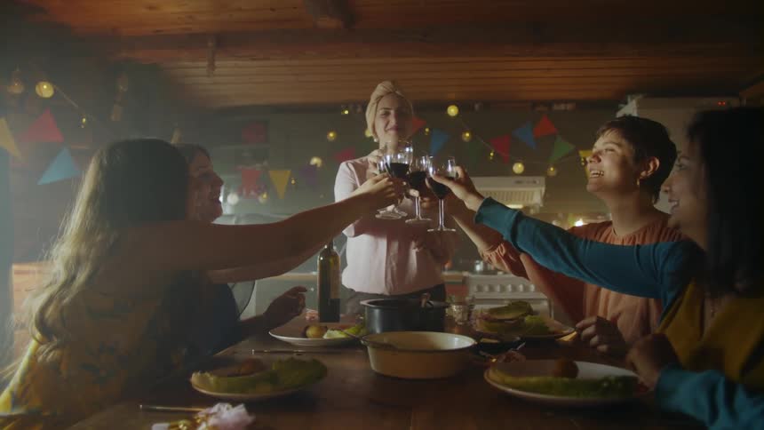 A woman talks at the head of a table while four other women sitting at the table clap in a room decorated for a party
