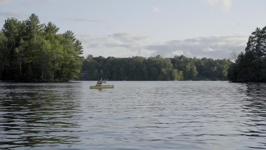 A person kayaks down a river that has thick forest to either side
