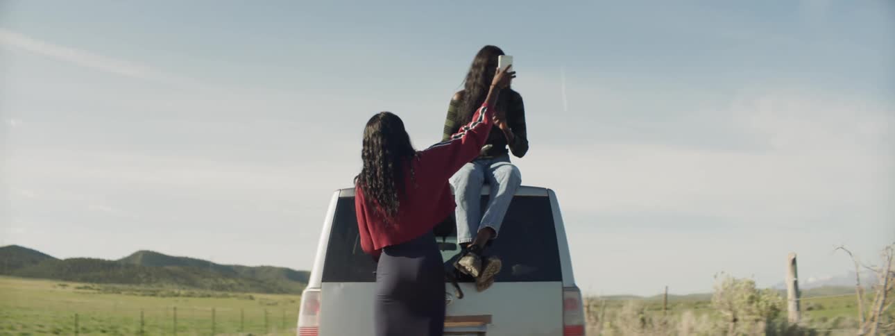 Woman takes picture on woman sitting on top of car