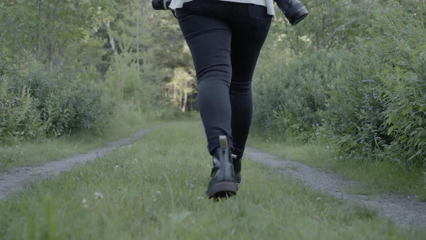 A female photographer is walking on a pathway in a natural setting in daylight