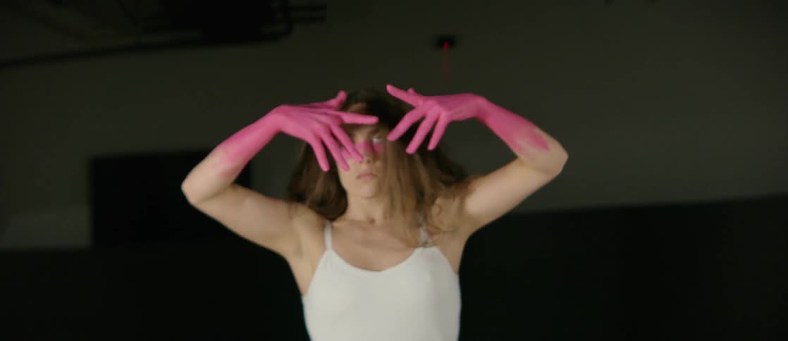 A woman with pink hands and forearms dances in front of darkness