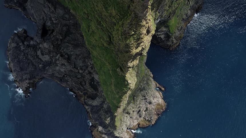 Birds fly around a tall cliff in the middle of a vast body of water