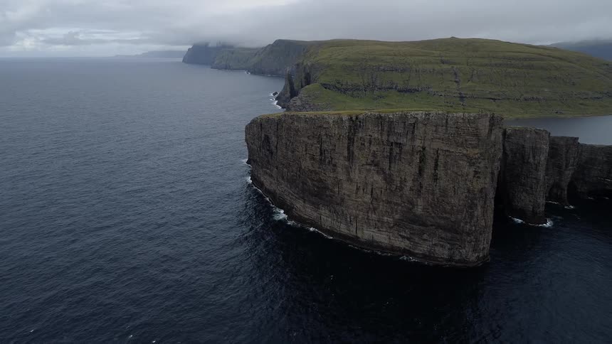 The ocean crashes onto the cliffs of a grass topped plateau